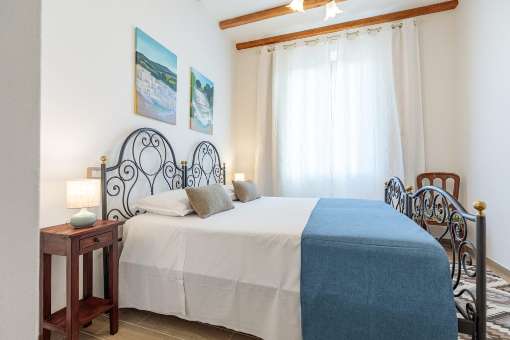 Camera matrimoniale di Villa Fontis Rapolano con letto in ferro battuto, soffitti in legno a vista, ampia finestra e ambienti luminosi per un soggiorno vicino alle Terme di Rapolano