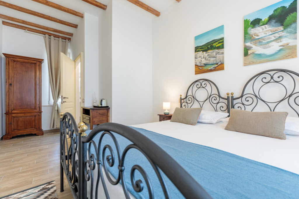 Camera doppia di Villa Fontis Rapolano con letti singoli unibili, soffitto con travi in legno, armadio, angolo cortesia con bollitore e dipinti ispirati alle Terme di San Giovanni e alle Terme di Saturnia