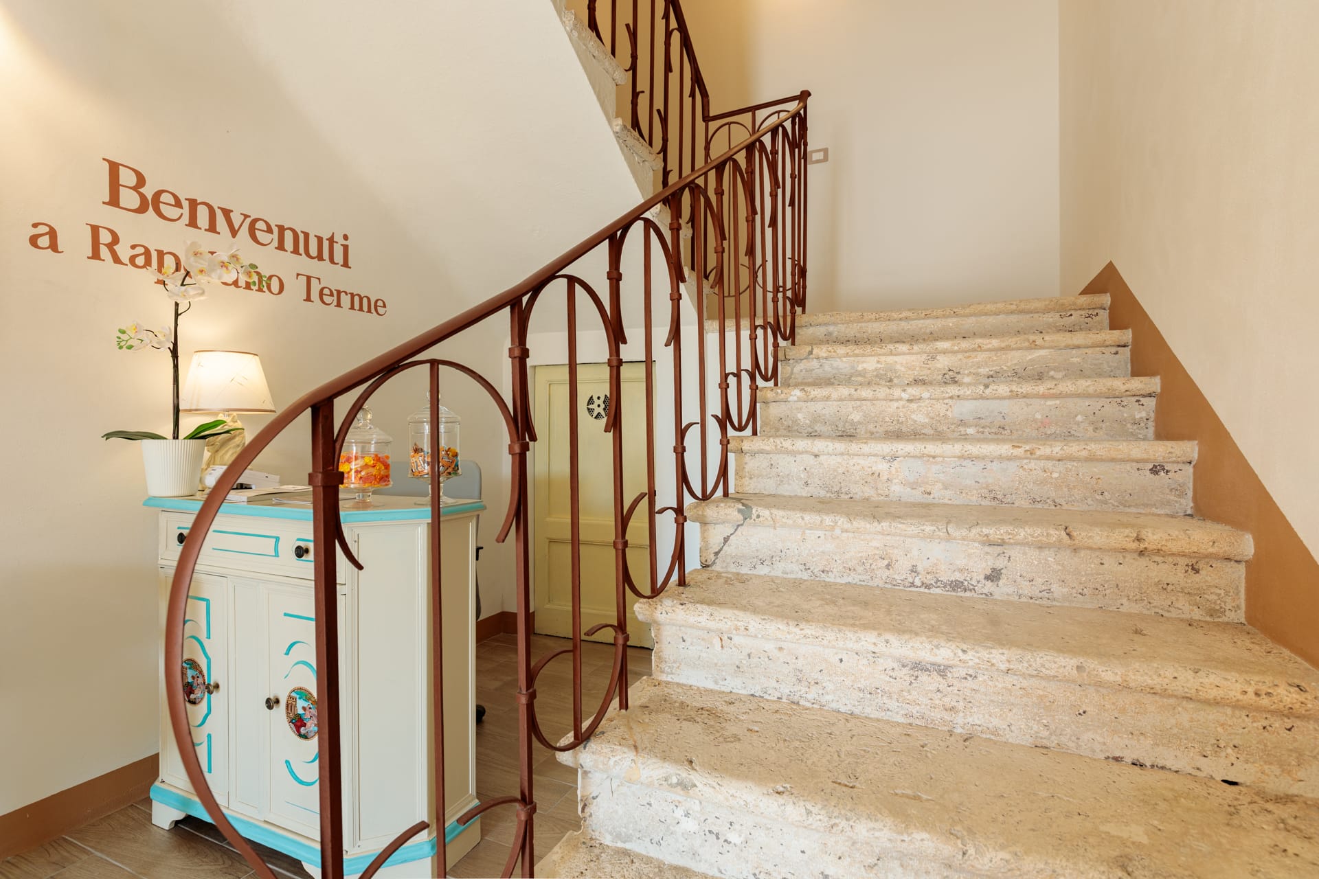 Scala interna di Villa Fontis Rapolano con ringhiera in ferro battuto, gradini in travertino e reception.