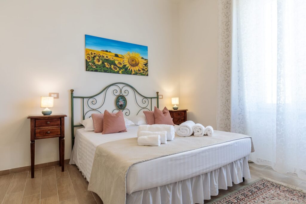 Camera matrimoniale elegante di Villa Fontis Rapolano con letto matrimoniale, asciugamani di cortesia, comodini in legno e ampia finestra vicino alle Terme di Rapolano