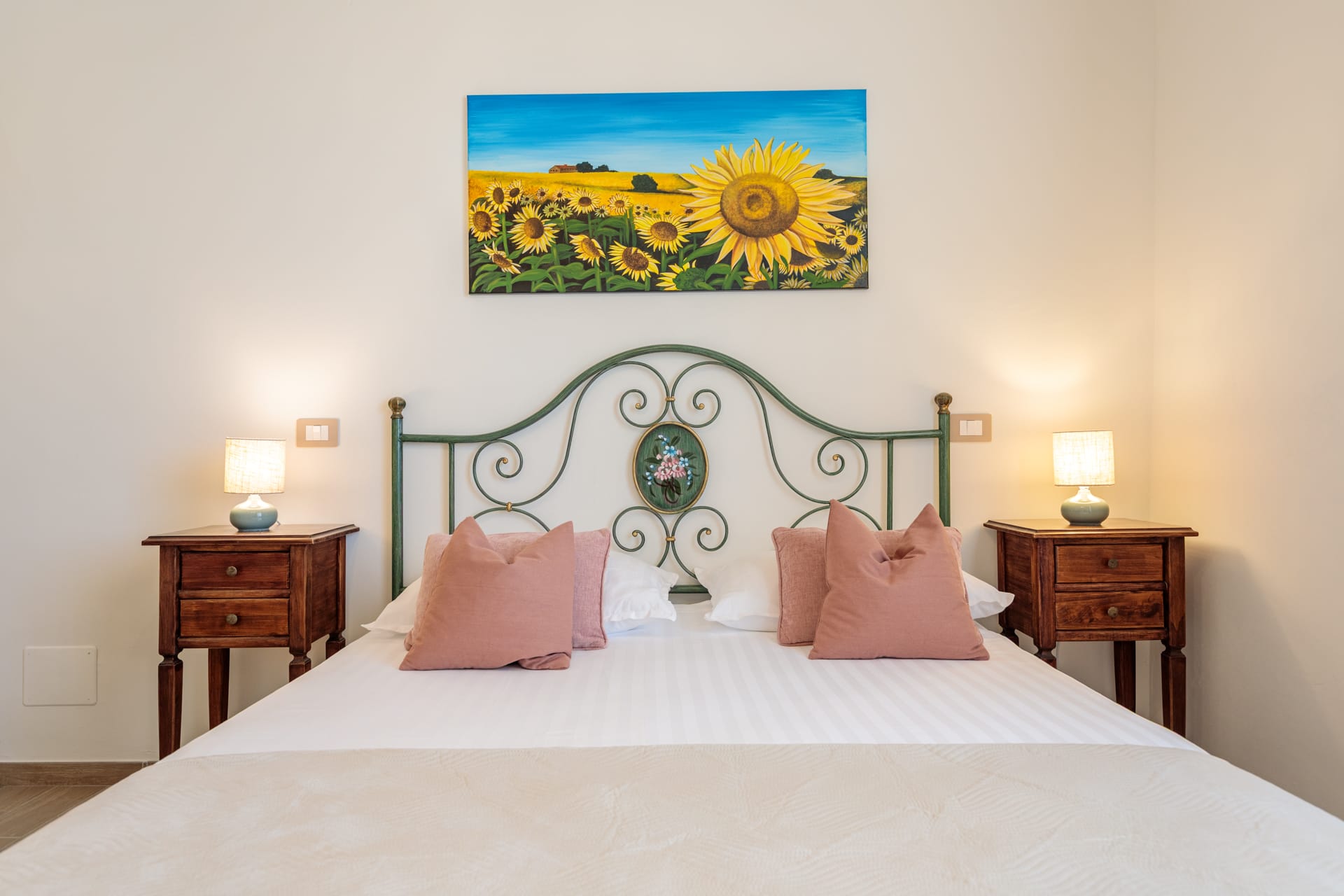 Camera matrimoniale di Villa Fontis Rapolano con letto in ferro battuto, comodini in legno e quadro di girasoli.