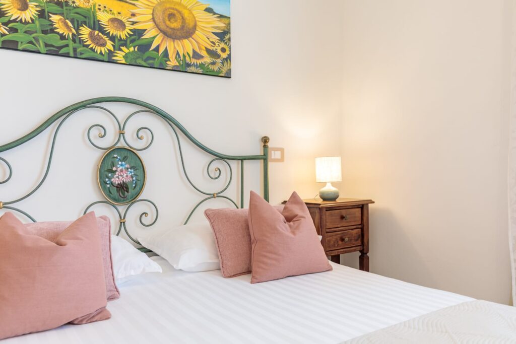 Camera matrimoniale di Villa Fontis Rapolano con letto matrimoniale, testiera in ferro battuto, comodino in legno e atmosfera rilassante vicino alle Terme di Rapolano