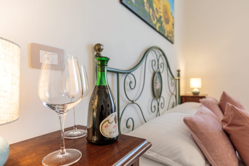 Dettaglio della camera matrimoniale di Villa Fontis Rapolano con calici e vino di benvenuto, letto matrimoniale e atmosfera accogliente a Rapolano Terme