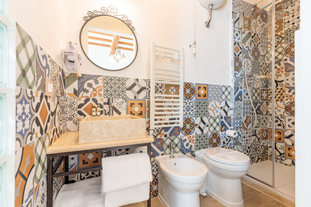 Bagno privato di Villa Fontis Rapolano con ampia doccia walk-in in vetro, lavabo in pietra naturale, scaldasalviette e rivestimenti decorativi in stile cementina