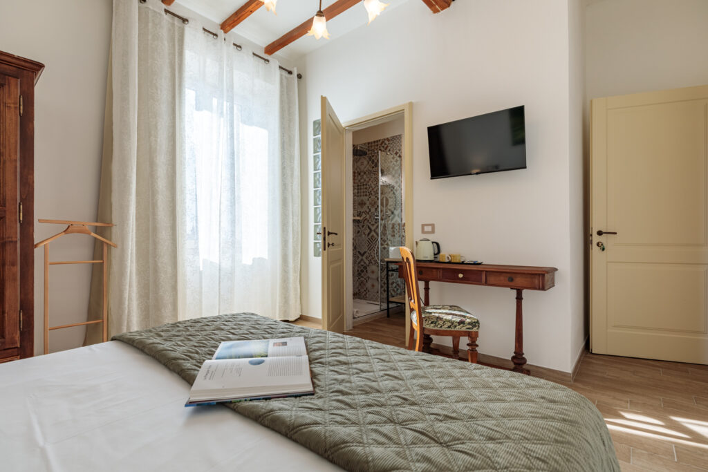 Camera matrimoniale di Villa Fontis Rapolano con letto king size, bagno privato con doccia, TV a schermo piatto, scrivania, bollitore per tè e caffè, soffitti con travi in legno e arredi in stile toscano.