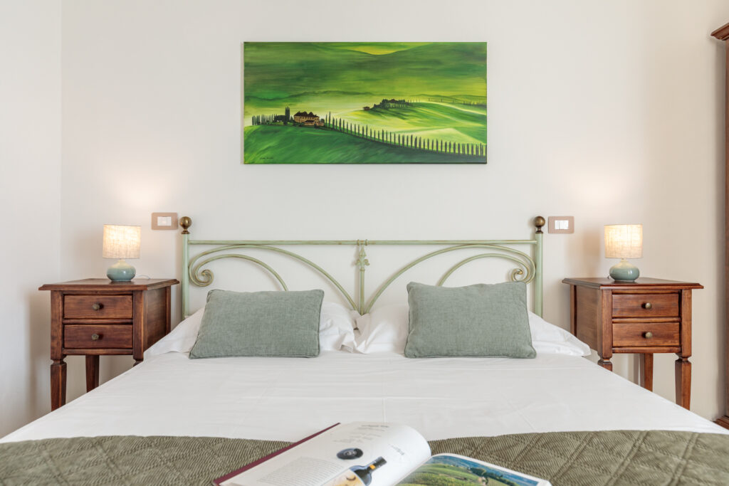 Camera matrimoniale di Villa Fontis Rapolano con letto in ferro battuto, comodini in legno, lampade, quadro raffigurante le colline toscane e atmosfera luminosa ed elegante.