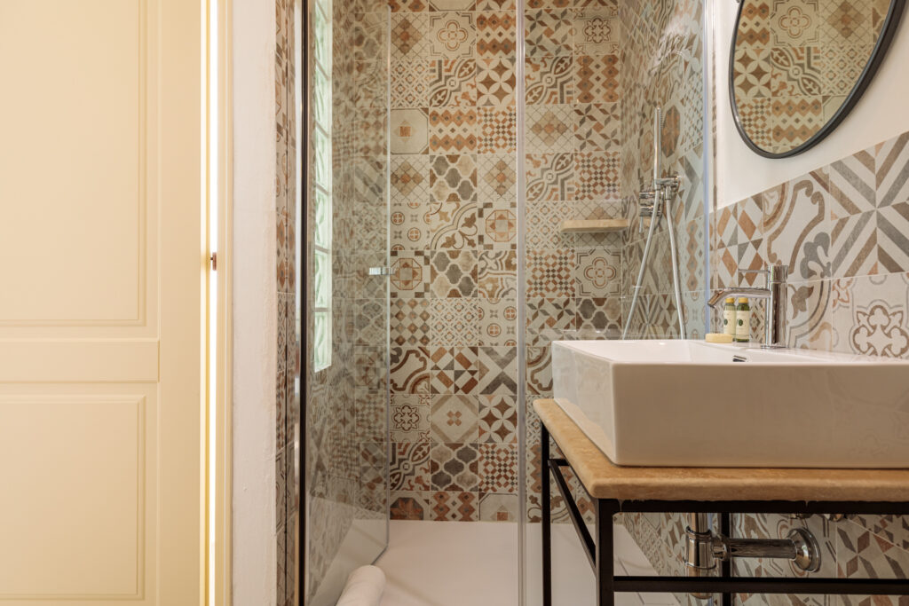 Bagno privato di Villa Fontis Rapolano con ampia doccia in vetro, lavabo moderno e rivestimenti in gres con motivi decorativi ispirati alle cementine