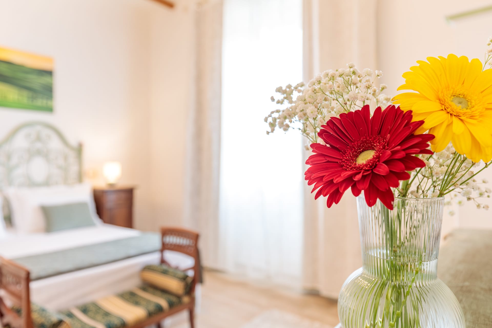 Camera di Villa Fontis Rapolano con ampia finestra luminosa, letto matrimoniale e fiori in primo piano.