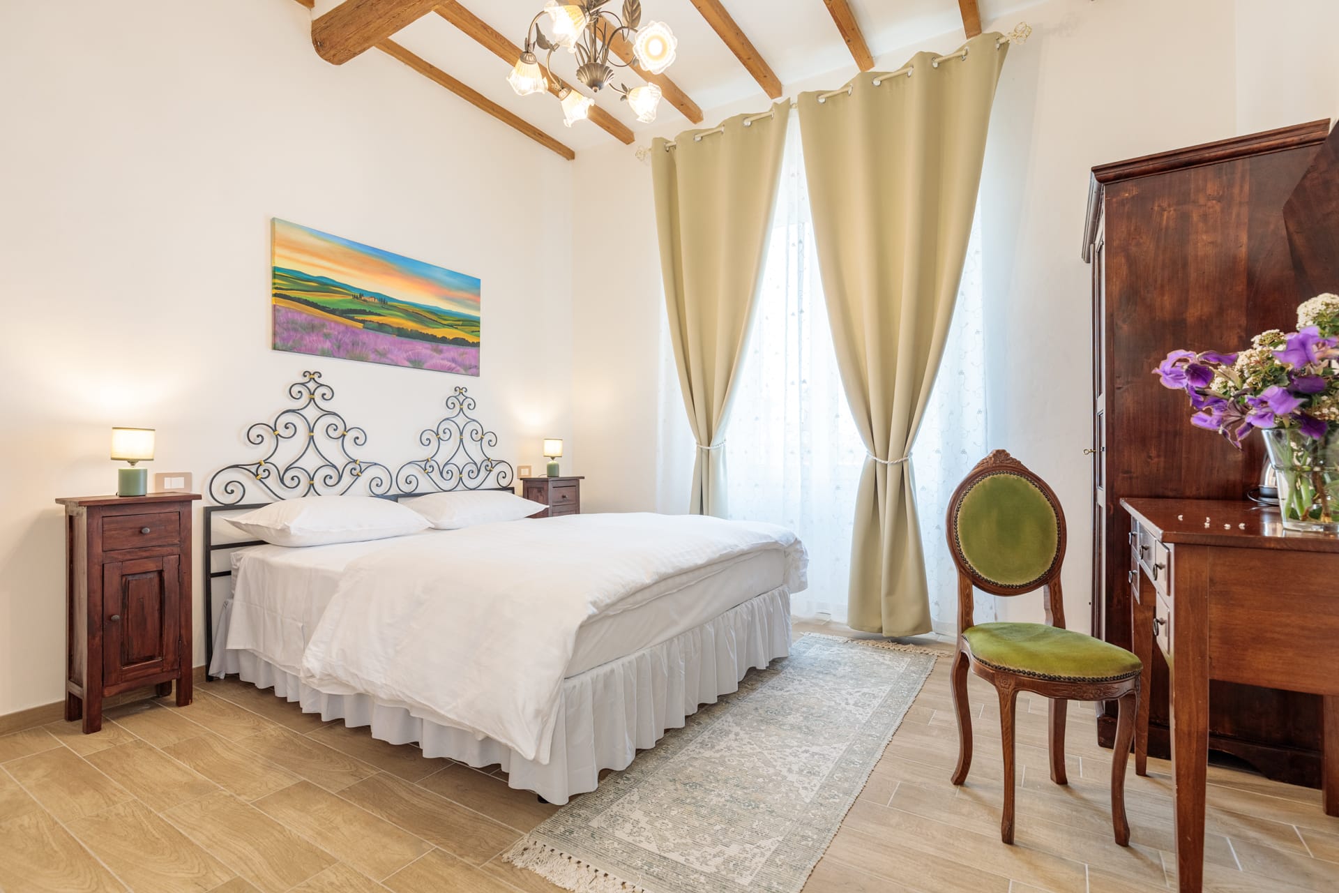 Camera matrimoniale Superior di Villa Fontis Rapolano con letto in ferro battuto, travi in legno e TV.