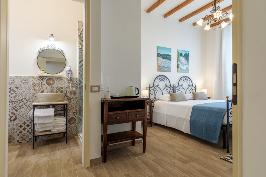 Vista d'insieme di una camera di Villa Fontis Rapolano con letti singoli unibili, bagno privato, angolo cortesia con bollitore, soffitto con travi in legno e arredi in stile toscano