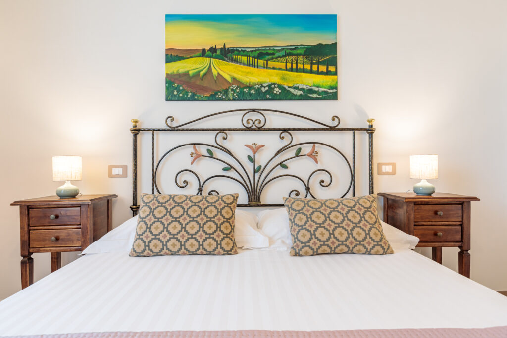 Letto matrimoniale della Camera Matrimoniale Comfort di Villa Fontis con testiera in ferro battuto e comodini in legno.